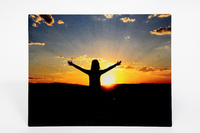 Individual with arms raised in front of a sunset.